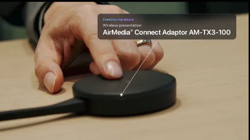 Hand pressing a Crestron AirMedia Connect Adaptor on a wooden desk