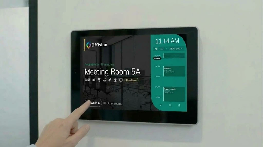 壁のパネルで Walk in をタップしている。Meeting Room 5A が46分間空いており、本日の予定も表示されている。